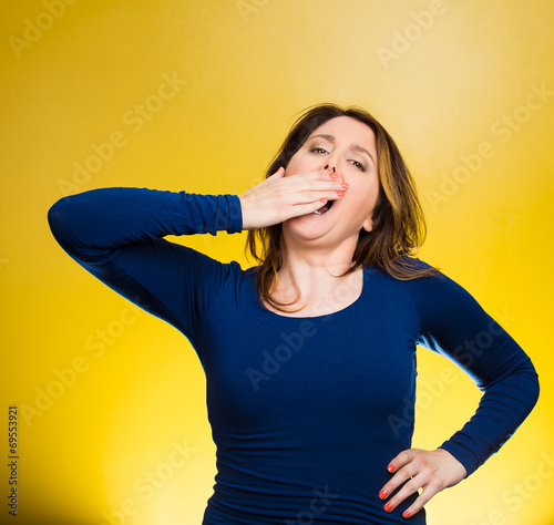 Sleep deprived young woman placing hand on mouth yawning