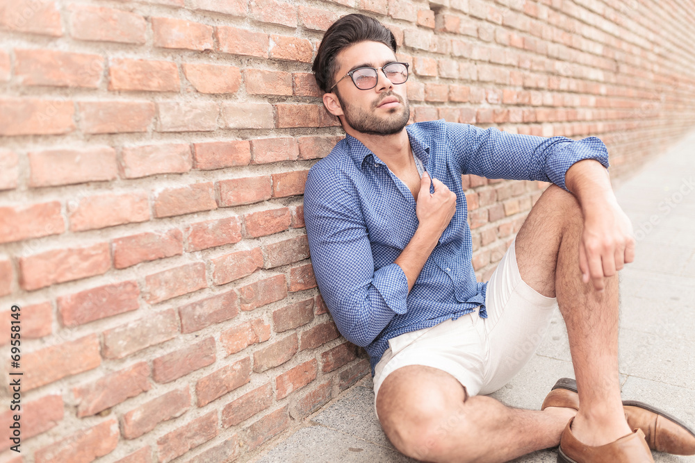 casual man sitting near brick wall looking up