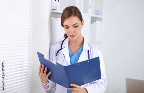 Young woman is standing in the near window with folder