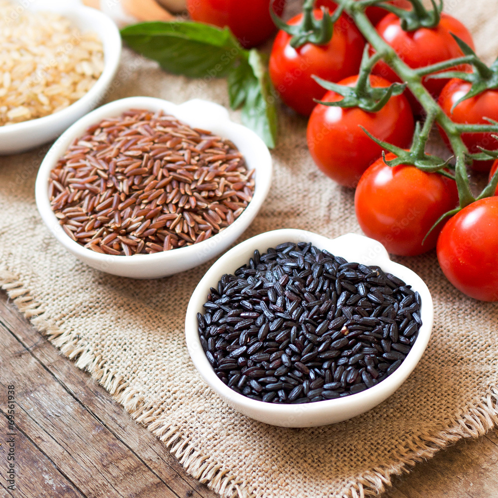 Variety of rice in bowls and tomatoes on wooden table Variety of rice in bowls and tomatoes on wooden table