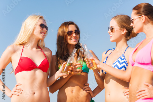 group of smiling young women drinking on beach