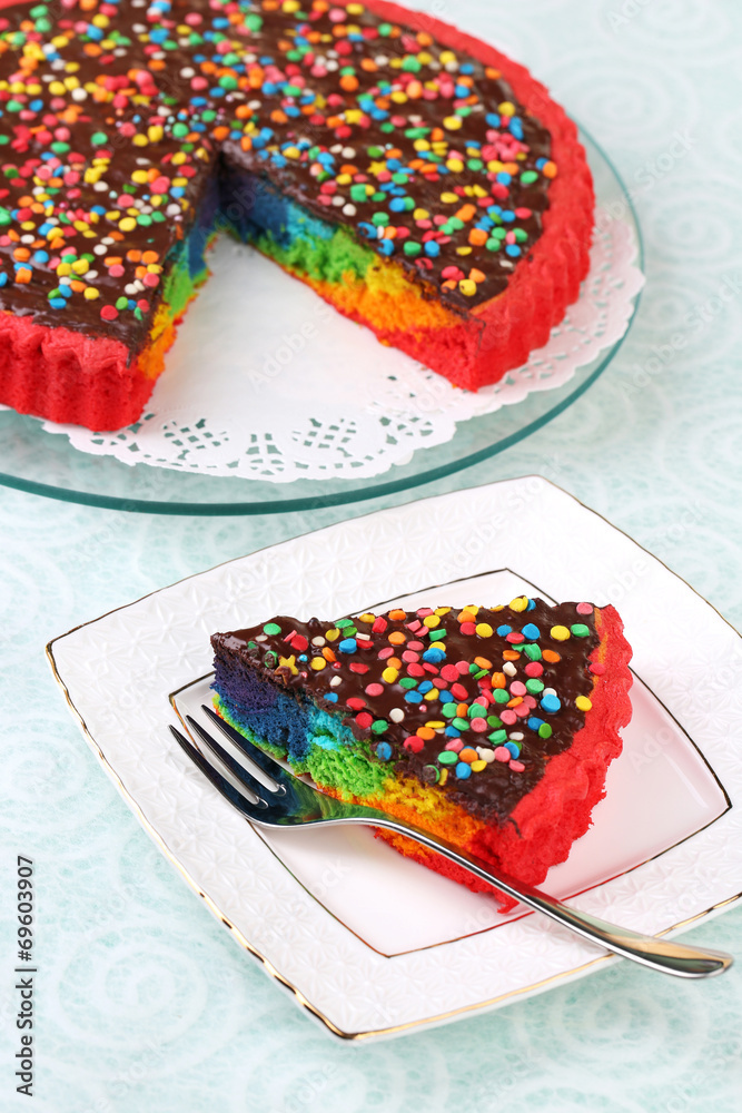 Delicious rainbow cake on plate, on tablecloth background Delicious rainbow cake on plate, on tablecloth background