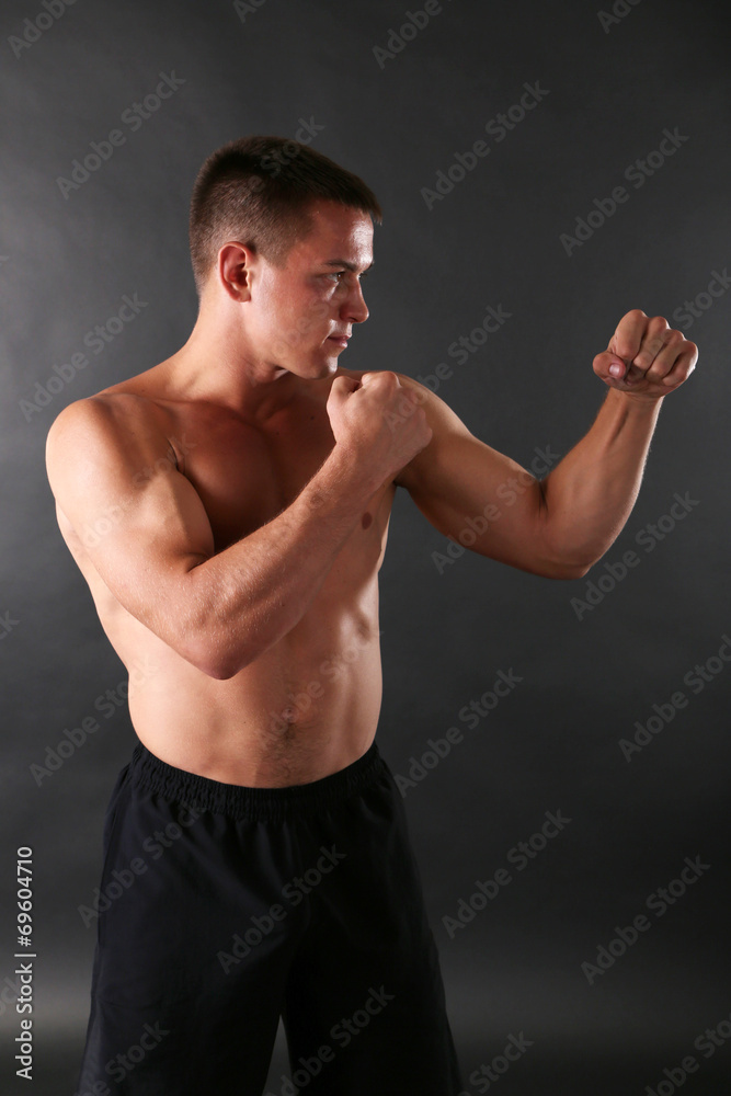 Handsome young muscular sportsman boxing on dark background