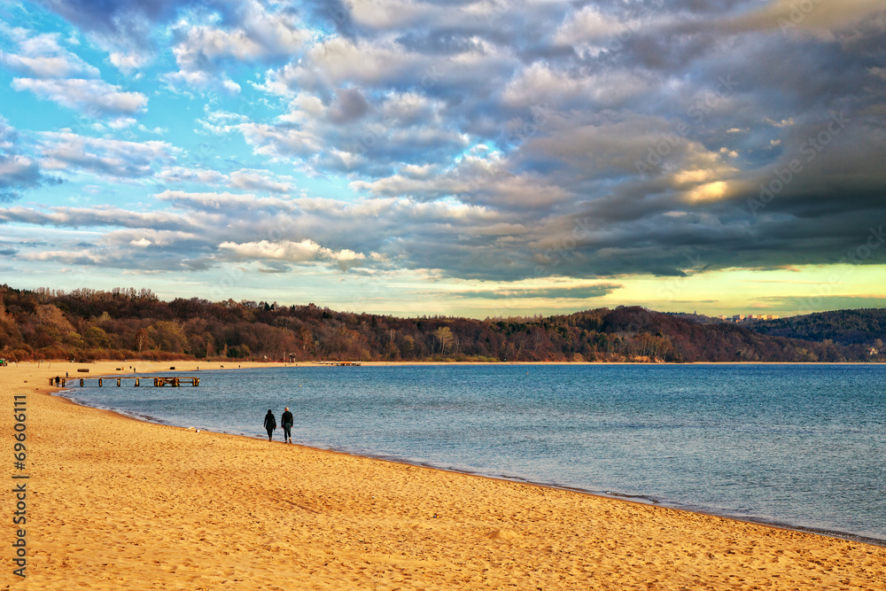 Fototapeta premium Couple walking on an empty beach a cloudy morning