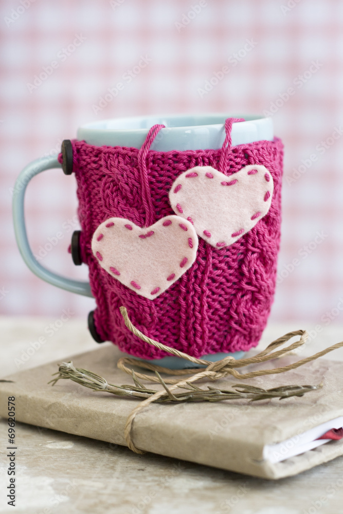Blue cup in pink sweater with felt hearts standing on notebook - obrazy, fototapety, plakaty 