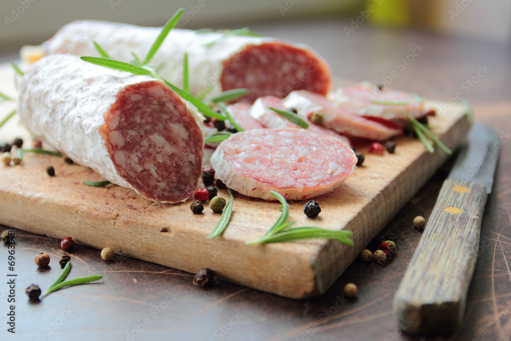 Sliced salami sausage on a wooden cutting board with herbs