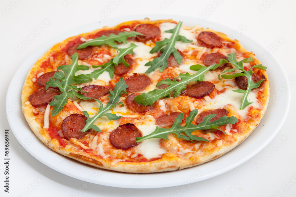 pizza with salami, cheese and arugula on white plate