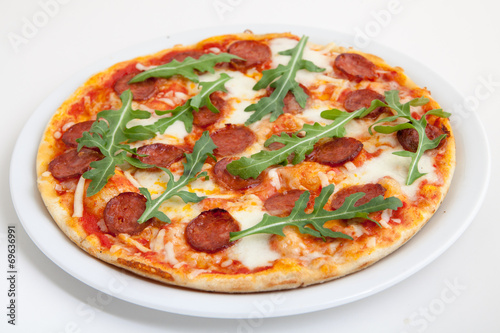 pizza with salami, cheese and arugula on white plate