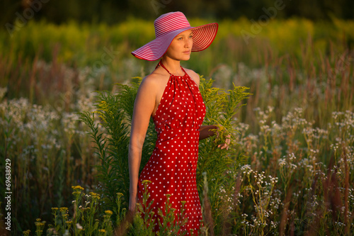 Εκτύπωση καμβά Elegant woman in a hat among wildflowers at sunset