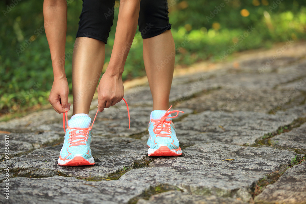 woman runner tying shoelace on stone trail