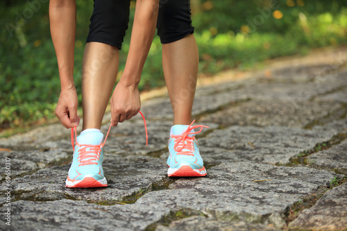 woman runner tying shoelace on stone trail