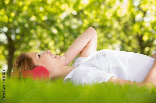 Pretty redhead lying on grass listening to music