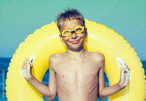 Funny chilld with swimmer goggles on beach with yellow float  photo