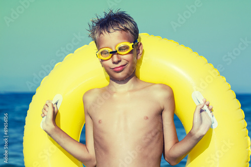 Funny chilld with swimmer goggles on beach with yellow float  photo