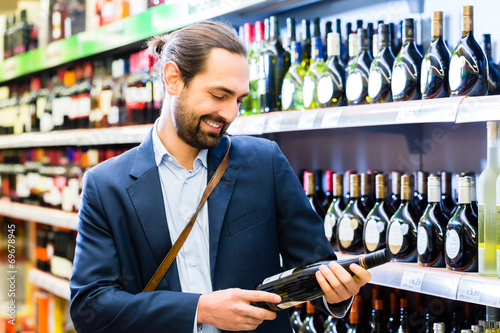Obraz na płótnie Mann wählt Wein im Supermarkt 