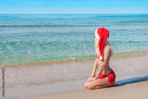 Beautiful blonde woman in red christmas hat on sea beach