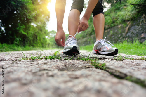 woman runner tying shoelace on stone trail