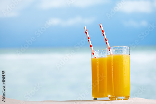 Two glasses of orange juice cocktail on white sandy beach
