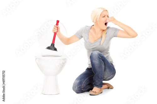 Obraz na plátně Woman unclogs a stinky toilet with plunger