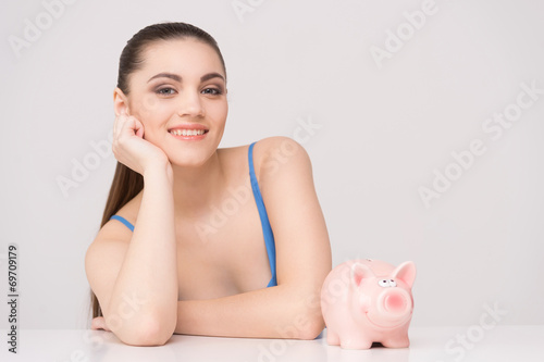 Happy female sitting at table with piggy bank. photo