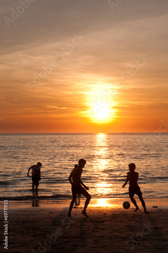 Sunset beach with teenagers playing football
