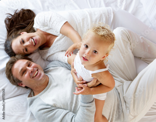 Family with cute little girl playing in bed
