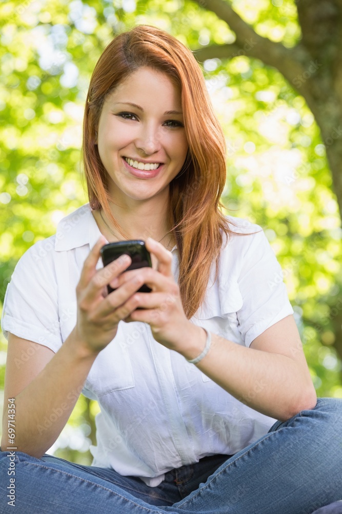 Pretty redhead sending a text in the park Pretty redhead sending a text in the park