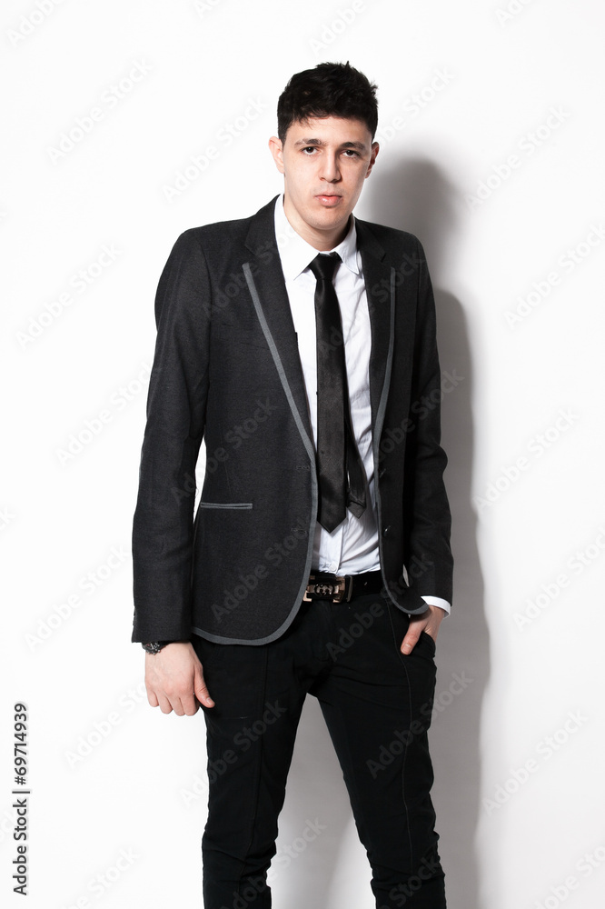 elegant man in black suit leaning against white wall at studio elegant man in black suit leaning against white wall at studio