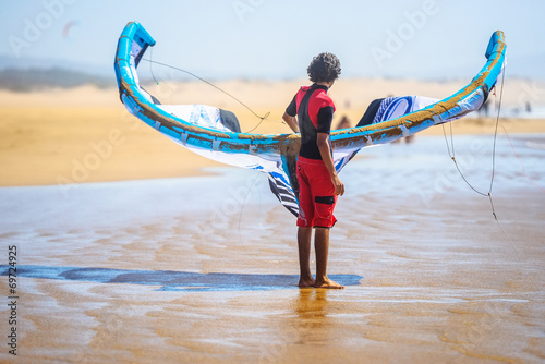 Photography A young man holding a surfing kite facing the sea
