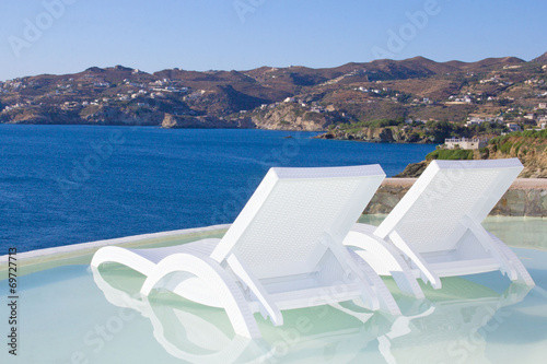 two white beach chairs in pool with sea view in Greece © Di Studio