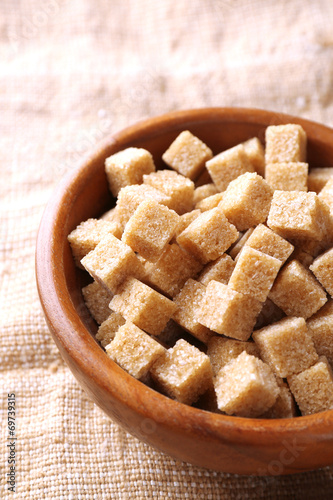 Brown sugar cubes in bowl on sackcloth background