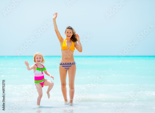 Mother and baby girl waving with hand on sea coast