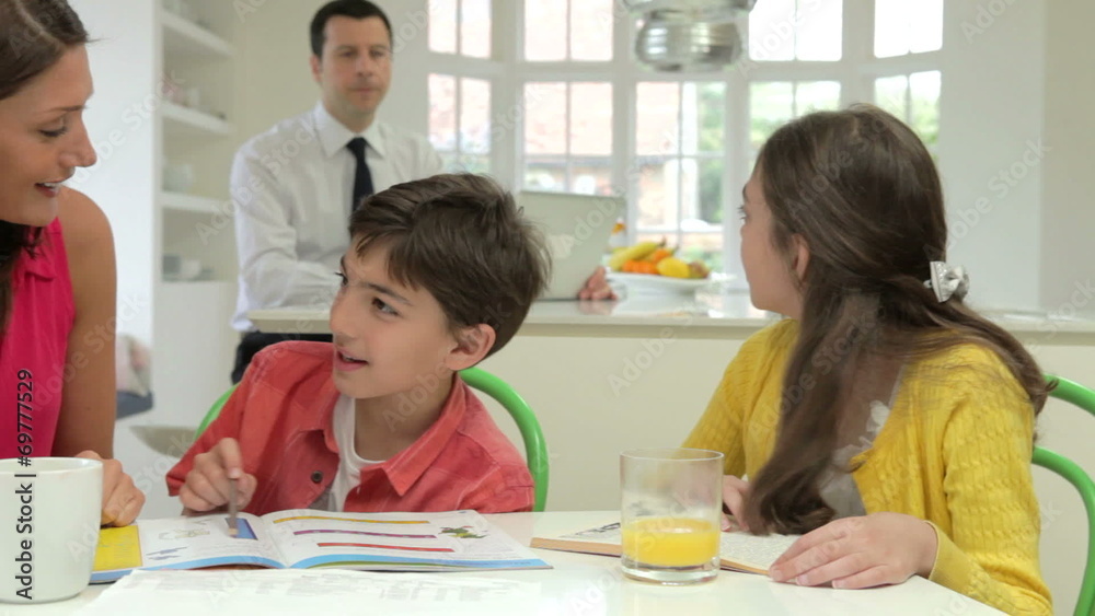 Mother Helping Children With Homework As Father Uses Laptop Mother Helping Children With Homework As Father Uses Laptop