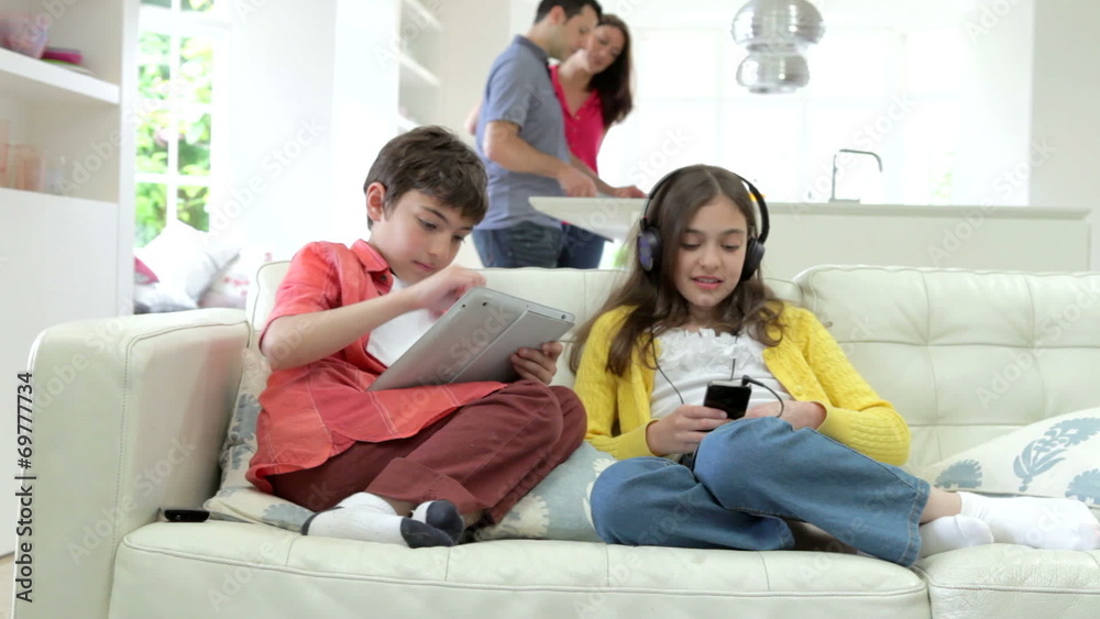 Children Playing With Digital Devices As Parents Make Meal Children Playing With Digital Devices As Parents Make Meal