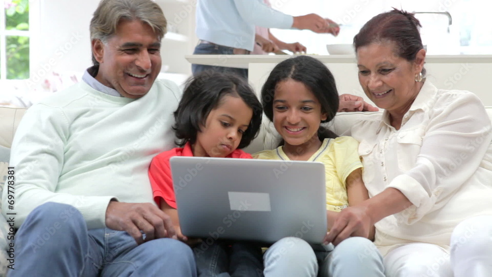 Multi-Generation Indian Family With Laptop Sitting On Sofa Multi-Generation Indian Family With Laptop Sitting On Sofa