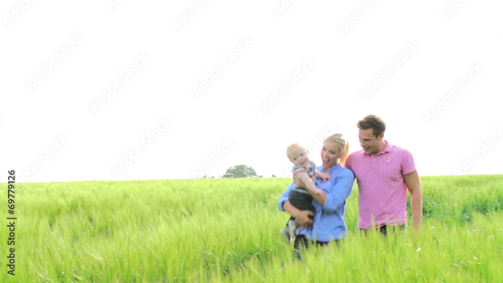 Family Walking In Field Carrying Young Baby Son Family Walking In Field Carrying Young Baby Son