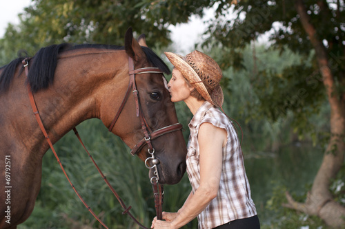 Woman in hat kissing the horse. © PaulShlykov
