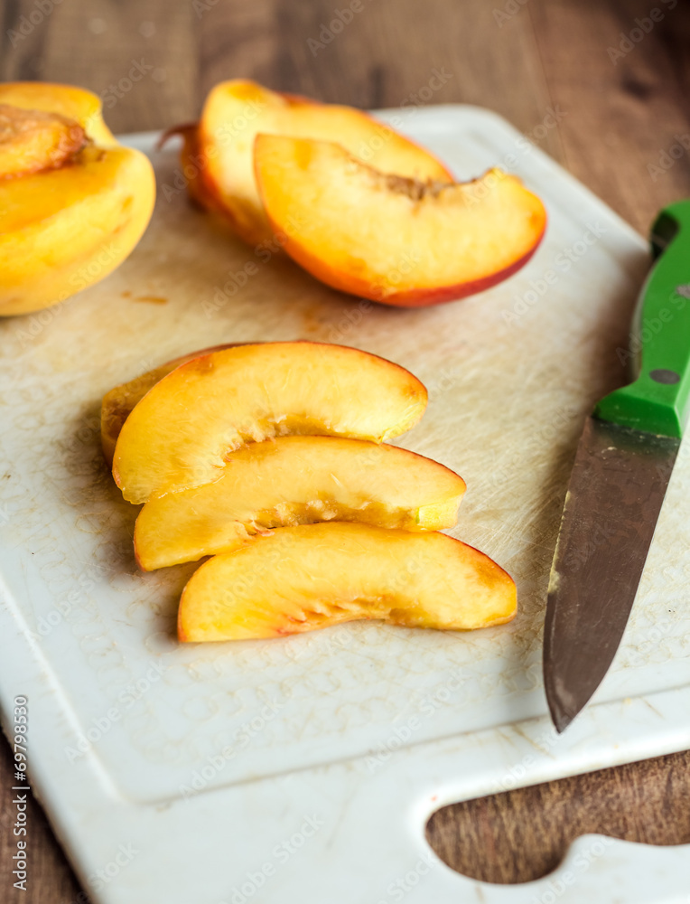 cut slices of ripe peach on a white board, green knife