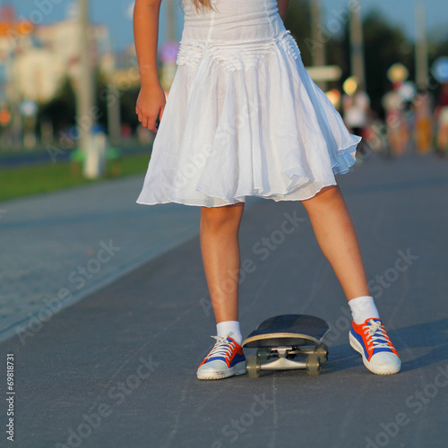teenager legs in sneakers with skateboard at sunset.