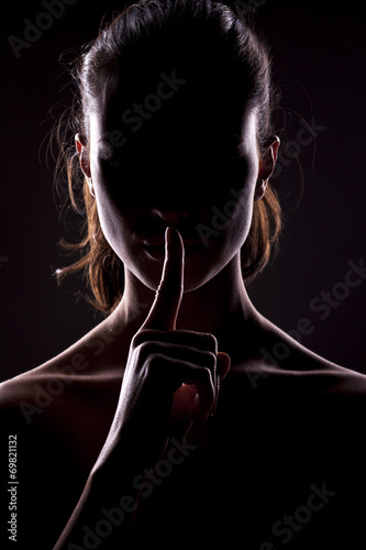 unknown woman with the face in the shadow holding finger on lips