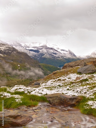 September snow on Alpine meadow, cascade on stream. © rdonar