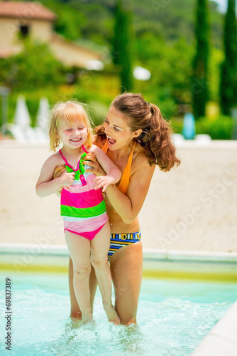 Happy mother and baby girl playing in swimming pool