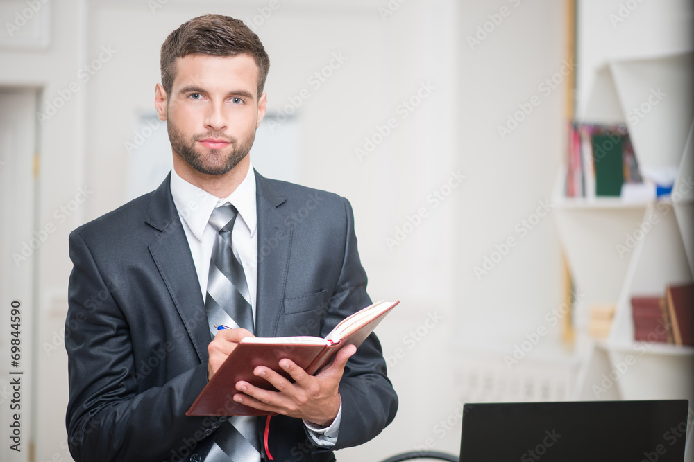 Portrait of handsome confident businessman writing in red notebo Portrait of handsome confident businessman writing in red notebo