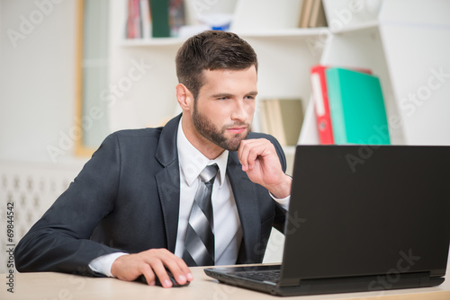 Businessman sitting at the table and working with laptop in offi