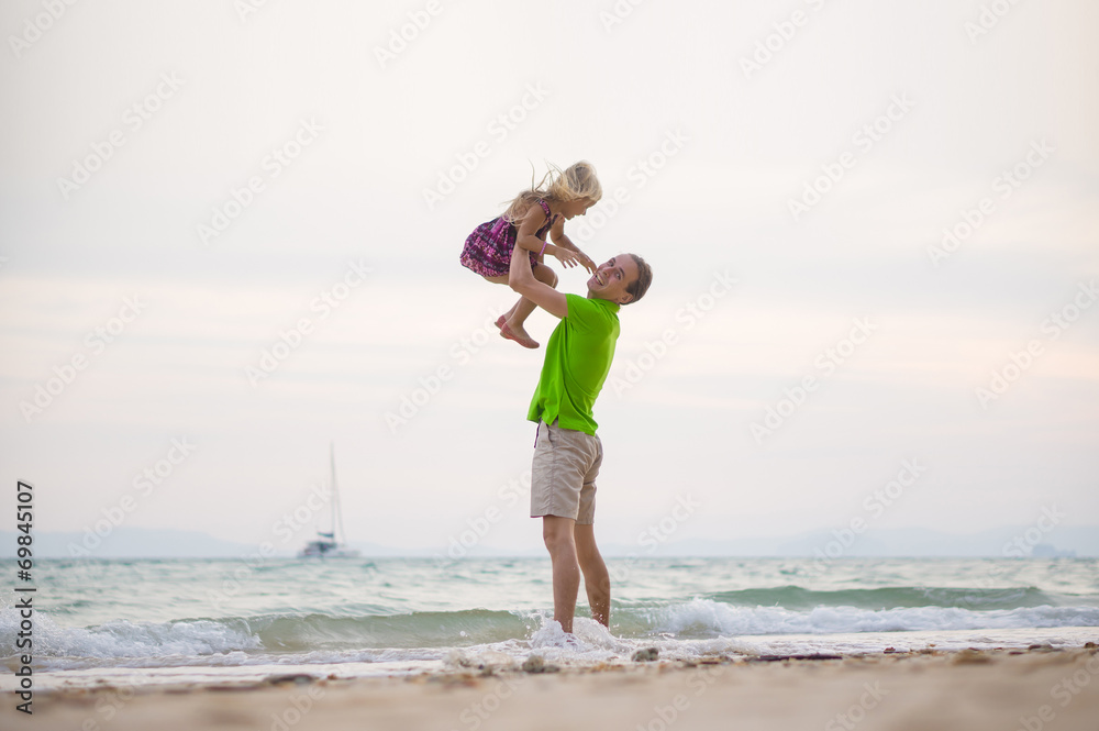 Father lift up daughter on hands on sunset ocean beach with yach