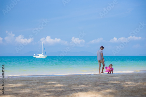Father and daughter in swimming suit play on ocean beach with ya