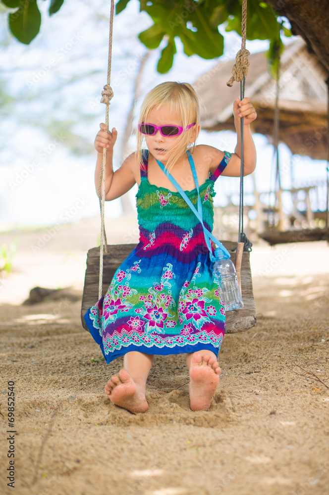 Adorable girl in sunglasses sit on rope swing under palm trees o Adorable girl in sunglasses sit on rope swing under palm trees o