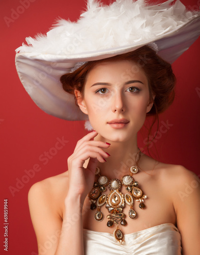 Obraz na plátně Portrait of redhead edwardian women with necklace on red backgro
