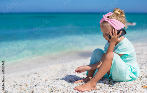 Little adorable girl talking at phone during beach vacation