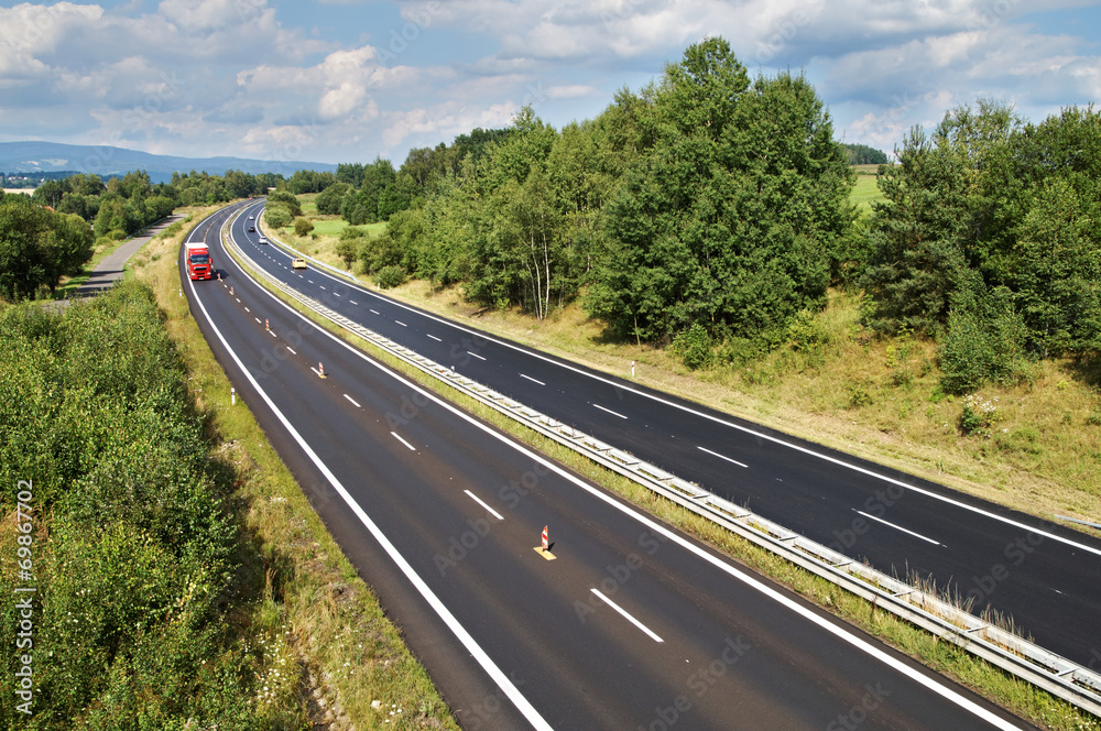 The rural landscape with a highway lined with trees, red truck